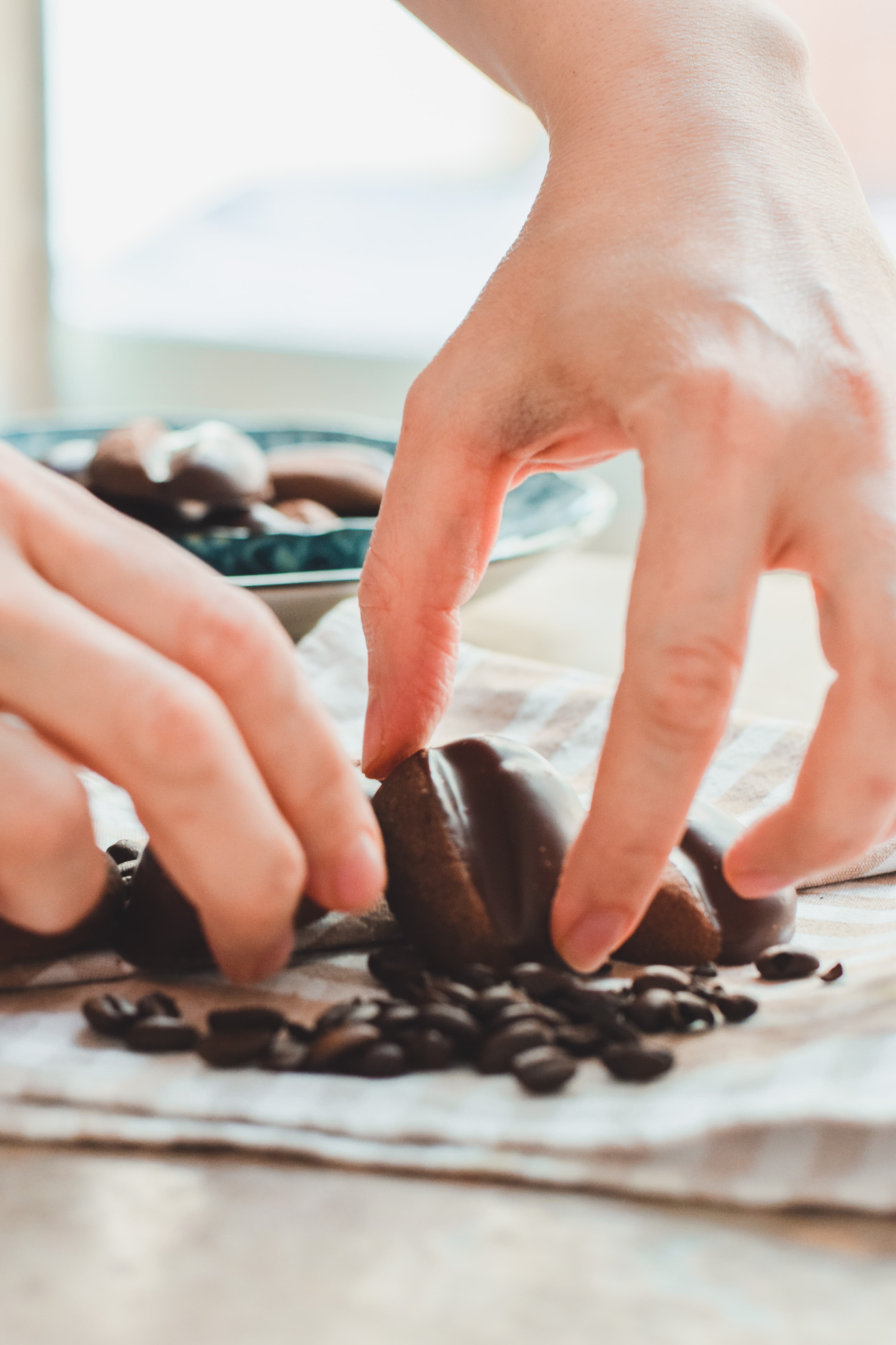 Hands placing biscuits among coffee beans on a linen cloth