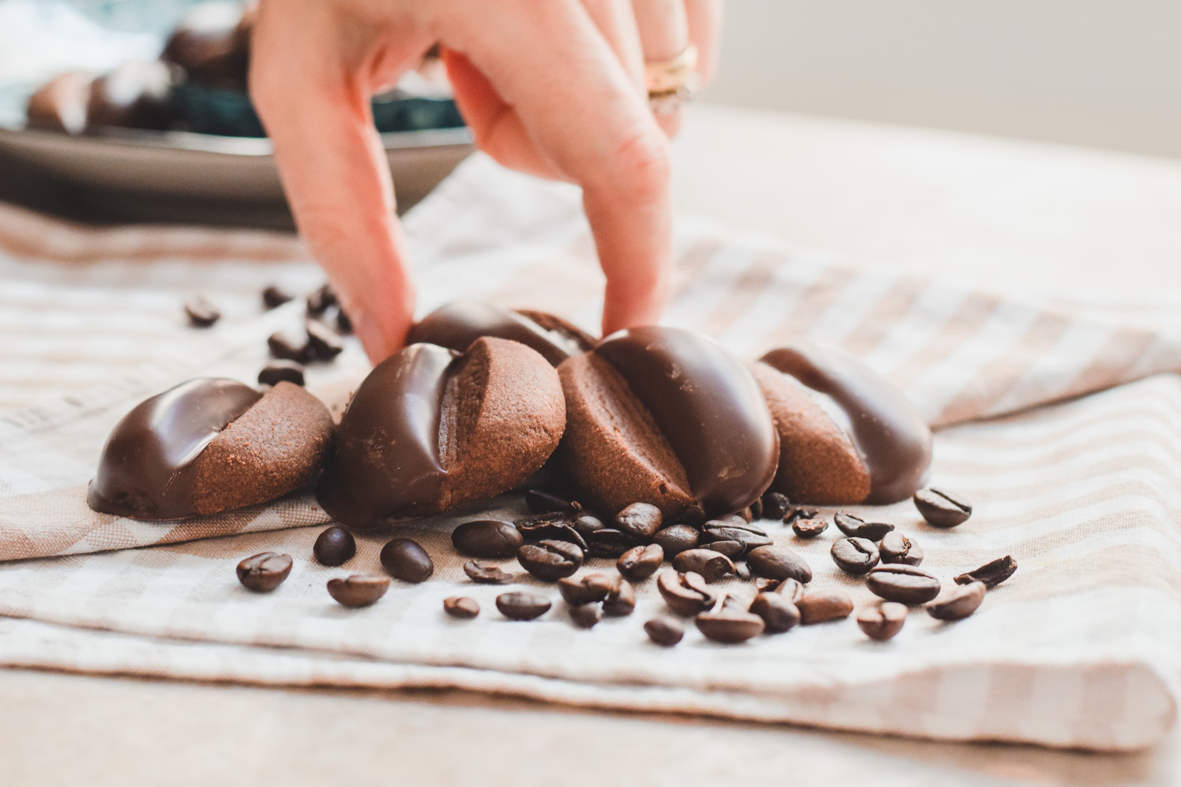 Hand reaching toward Reena Bakes cookies among coffee beans