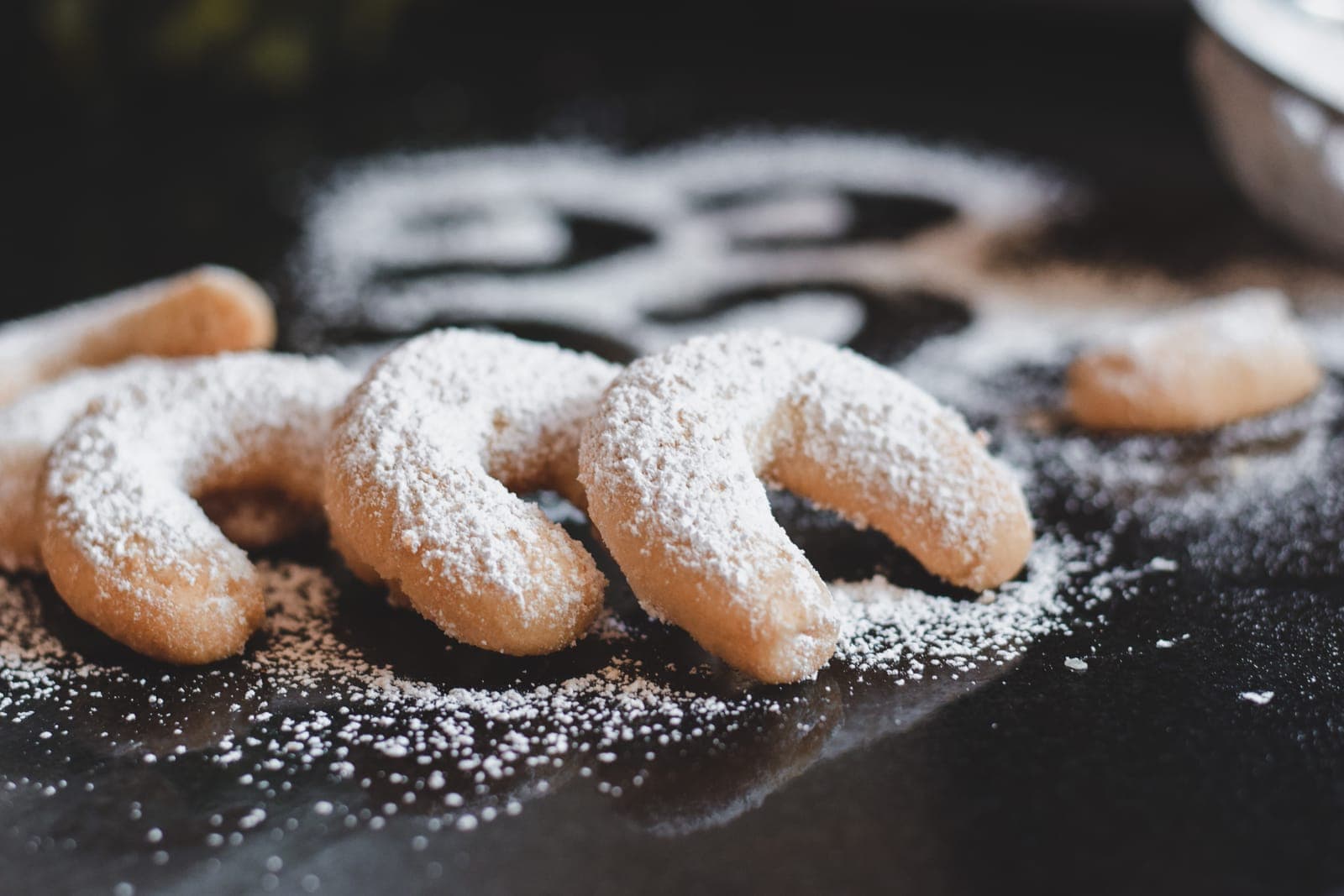 Three Vanilla Almond crescent cookies dusted with powdered sugar on a dark surface